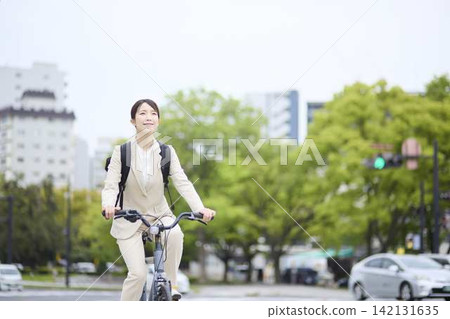 一位女商人騎著腳踏車在市中心穿梭。 一位女商人騎著腳踏車在市中心穿梭。 142131635