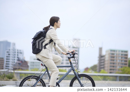 一位女商人騎著自行車穿梭在綠樹成蔭的城市。 一位女商人騎著自行車穿梭在綠樹成蔭的城市。 142131644