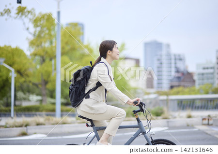一名女子騎著自行車穿過城市街道。 一名女子騎著自行車穿過城市街道。 142131646