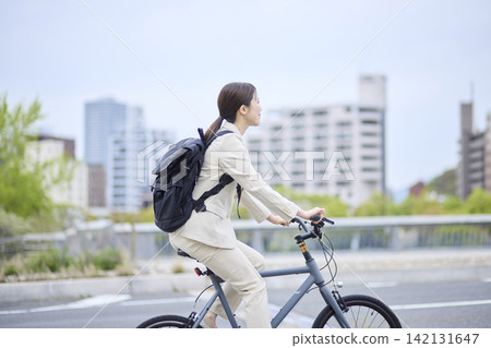 一位女子騎著自行車通勤，背景是都會景觀。 142131647