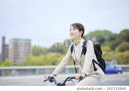 A businesswoman riding a bicycle through the city (front view) A businesswoman riding a bicycle through the city (front view) 142131648