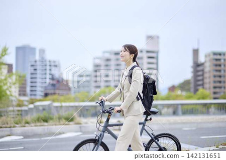 一位女商人推著自行車走在城市裡。 一位女商人推著自行車走在城市裡。 142131651