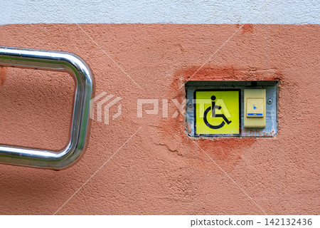 Disabled call button assistance system near an accessible wheelchair ramp. Yellow handicap symbol sign on a textured concrete wall Disabled call button assistance system near an accessible wheelchair ramp. Yellow handicap symbol sign on a textured concrete wall 142132436