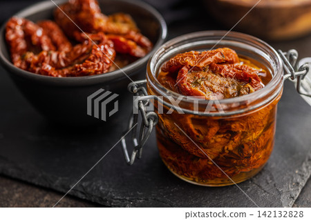 Sun-Dried Tomatoes in Jar with Olive Oil on Slate Board, Rustic Preserved Tomato Close-Up Sun-Dried Tomatoes in Jar with Olive Oil on Slate Board, Rustic Preserved Tomato Close-Up 142132828