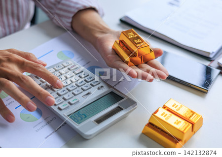 Investor hand using calculator for gold bar trading analysis. Concept for wealth management, asset protection, and financial planning. 142132874