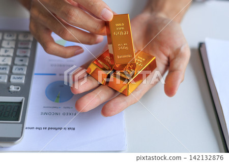 Physical gold bars on investor's hand at office desk. Concept for secure financial investment and wealth preservation. Physical gold bars on investor's hand at office desk. Concept for secure financial investment and wealth preservation. 142132876