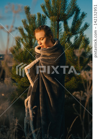 Woman wrapped in cozy blanket among pine trees at golden hour Woman wrapped in cozy blanket among pine trees at golden hour 142132951