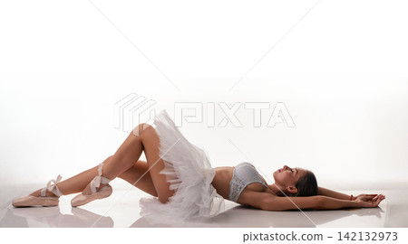 Ballerina in white tutu lying on studio floor with arms extended Ballerina in white tutu lying on studio floor with arms extended 142132973