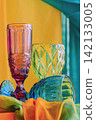 Scenic vivid vintage glassware, bright fabric against vibrant orange and turquoise background. Colorful Glassware Art Still Life with Vibrant Maximalist Decor setting, textured glasses, bold colors 142133005