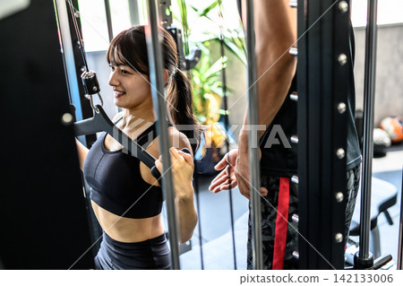 A woman working out with a lat pulldown machine, receiving instructions from a trainer at the gym; daytime colors are clearly visible. A woman working out with a lat pulldown machine, receiving instructions from a trainer at the gym; daytime colors are clearly visible. 142133006