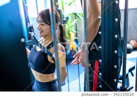 A woman working out with a lat pulldown machine, receiving instructions from a trainer at the gym. 142133010