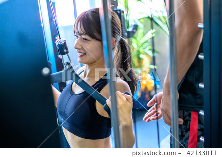 一位女士正在健身房使用下拉器材鍛煉,教練正在指導她。 一位女士正在健身房使用下拉器材鍛煉,教練正在指導她。 142133011