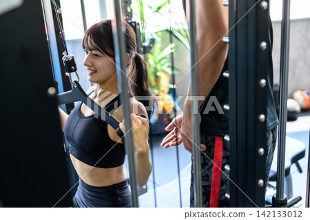 一位女士正在健身房使用下拉器材鍛煉,並接受教練的指導。 (普通領口) 一位女士正在健身房使用下拉器材鍛煉,並接受教練的指導。 (普通領口) 142133012