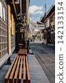 A wooden bench placed in front of a townhouse with a lattice door. 142133154
