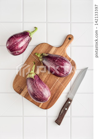 Three fresh purple eggplants on wooden cutting board Three fresh purple eggplants on wooden cutting board 142133397