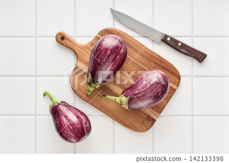 Three fresh purple eggplants on wooden cutting board Three fresh purple eggplants on wooden cutting board 142133398