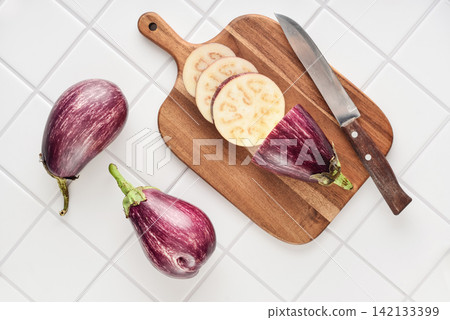 Three fresh purple eggplants on wooden cutting board Three fresh purple eggplants on wooden cutting board 142133399