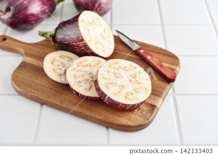 Three fresh purple eggplants on wooden cutting board Three fresh purple eggplants on wooden cutting board 142133403