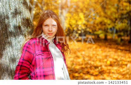 Young woman stands by a tree in a forest during autumn with colorful leaves on the ground Young woman stands by a tree in a forest during autumn with colorful leaves on the ground 142133451