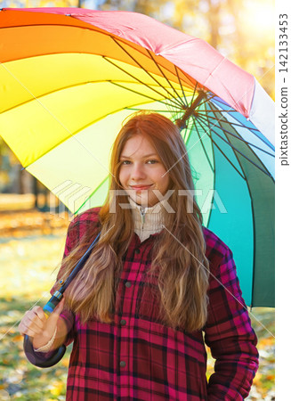Young person holds a colorful umbrella in a park during sunny weather in autumn Young person holds a colorful umbrella in a park during sunny weather in autumn 142133453