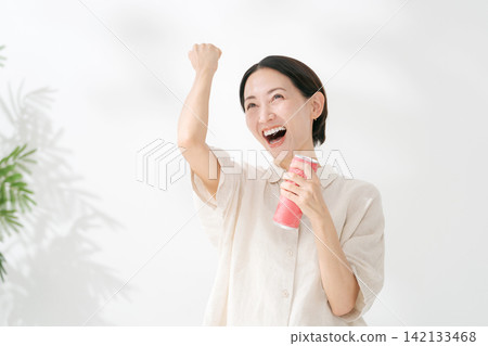 A woman makes a victory pose and drinks her beverage. A woman makes a victory pose and drinks her beverage. 142133468