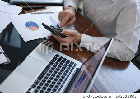 Businessman, accountant, financier using calculator to work through financial documents, report, charts and data on desk Businessman, accountant, financier using calculator to work through financial documents, report, charts and data on desk 142133802