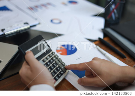 Businessman, accountant, financier using calculator to work through financial documents, report, charts and data on desk 142133803