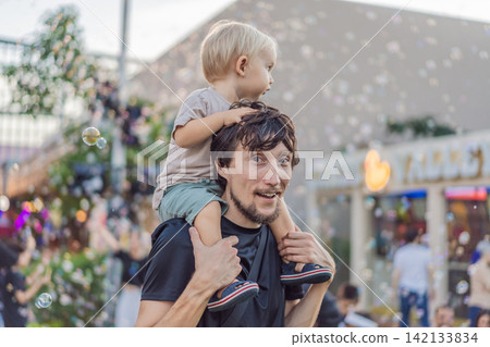 Dad smiles with a three year old child among colorful holiday decorations, showing fatherhood, family celebration and festive outing concept Dad smiles with a three year old child among colorful holiday decorations, showing fatherhood, family celebration and festive outing concept 142133834