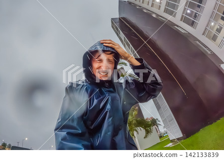 Adult man faces heavy rain and strong wind near palm trees and city buildings, showing storm weather, hurricane season and climate resilience concept Adult man faces heavy rain and strong wind near palm trees and city buildings, showing storm weather, hurricane season and climate resilience concept 142133839