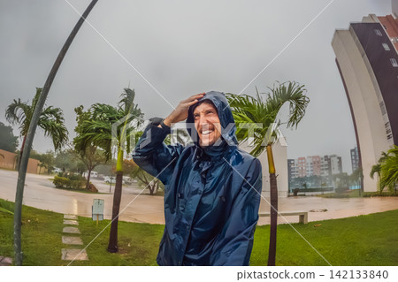 Adult man faces heavy rain and strong wind near palm trees and city buildings, showing storm weather, hurricane season and climate resilience concept Adult man faces heavy rain and strong wind near palm trees and city buildings, showing storm weather, hurricane season and climate resilience concept 142133840
