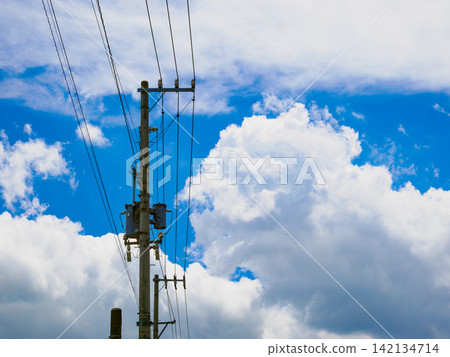 A summer scene with towering cumulonimbus clouds and telephone poles against a clear blue sky. A summer scene with towering cumulonimbus clouds and telephone poles against a clear blue sky. 142134714