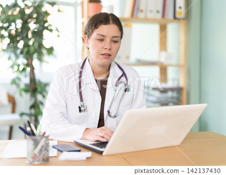 Young female doctor searches for information on the internet using laptop in the office of medical clinic Young female doctor searches for information on the internet using laptop in the office of medical clinic 142137430