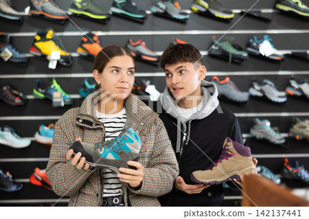 Married couple choose winter trekking shoes together in sports shop 142137441
