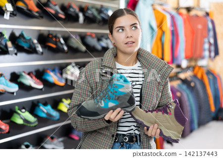 Girl examine compare item of winter comfortable tracking shoes Girl examine compare item of winter comfortable tracking shoes 142137443
