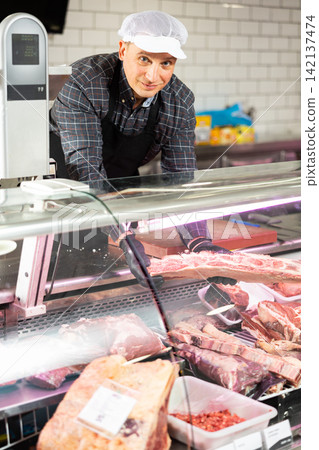 Confident male butcher showing a big piece of beef ribs in butchery Confident male butcher showing a big piece of beef ribs in butchery 142137474