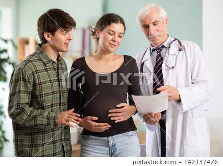 Happy young couple listening elderly doctor's advises about good pregnancy Happy young couple listening elderly doctor's advises about good pregnancy 142137476