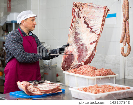 Positive male butcher preparing big piece of beef meat in butcher shop Positive male butcher preparing big piece of beef meat in butcher shop 142137548