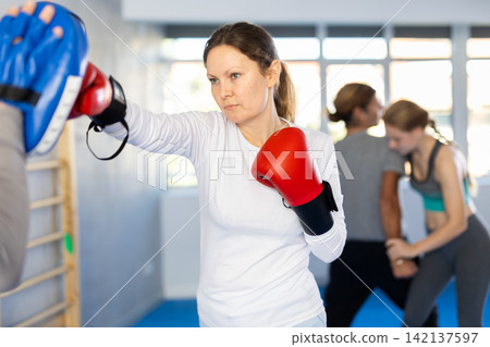 Woman works out strength and speed of boxing punch mitts with help of partner in boxing paws Woman works out strength and speed of boxing punch mitts with help of partner in boxing paws 142137597