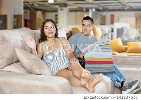Smiling woman and man choosing upholstery for sofa in furnishing store 142137613