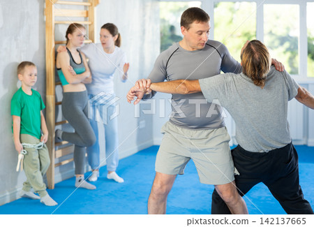 Man with trainer in self-defense training in gym practices trip up opponent during sparring Man with trainer in self-defense training in gym practices trip up opponent during sparring 142137665