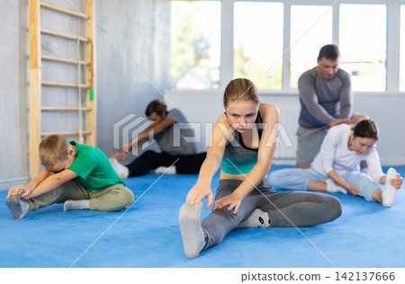 Family in gym during group sports training under guidance of trainer performs stretching on floor 142137666