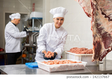 Smiling female butcher making ground beef in butcher shop Smiling female butcher making ground beef in butcher shop 142137667