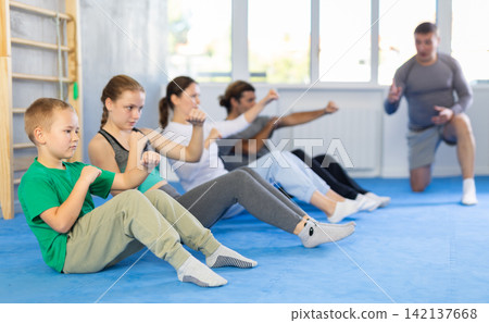 Group of people performing combat strikes sitting during group training Group of people performing combat strikes sitting during group training 142137668