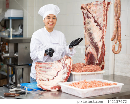 Butchery workwoman preparing meat for sale at cutting table Butchery workwoman preparing meat for sale at cutting table 142137672
