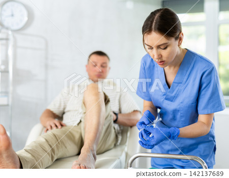 Young woman doctor doing knee injection for the patient lying on clinical chair Young woman doctor doing knee injection for the patient lying on clinical chair 142137689