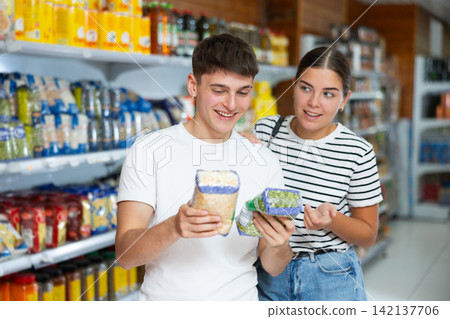 Girl and guy are standing in supermarket and choosing pack of pea cereals 142137706