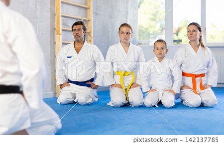 Group of people in kimono with master in sitting position during group karate training Group of people in kimono with master in sitting position during group karate training 142137785