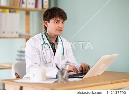 Experienced young male doctor therapist working at hospital laptop sitting in office at workplace Experienced young male doctor therapist working at hospital laptop sitting in office at workplace 142137790