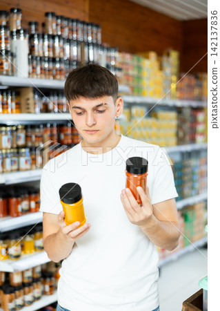 Guy chooses jars of spices in the grocery department of hypermarket Guy chooses jars of spices in the grocery department of hypermarket 142137836