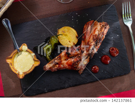 Roast rabbit served with potatoes and braised peppers 142137861